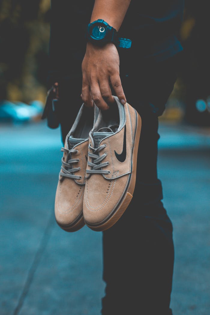 A person outdoors holding beige Nike sneakers, showcasing style and urban fashion.