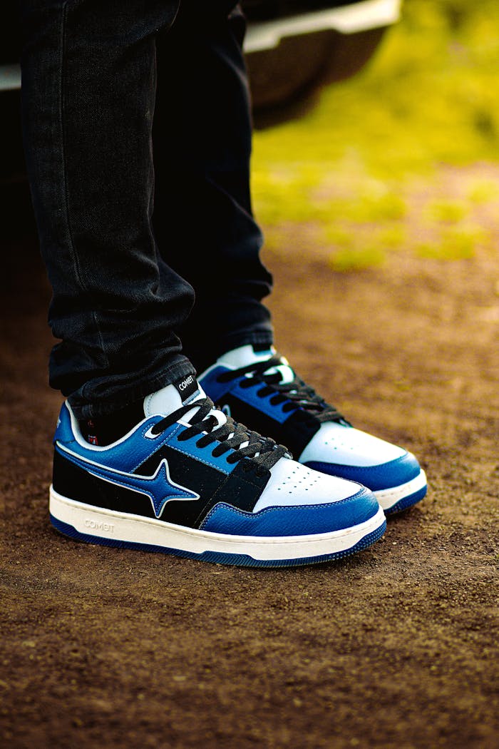 Close-up of trendy blue sneakers worn outdoors on a dirt path.